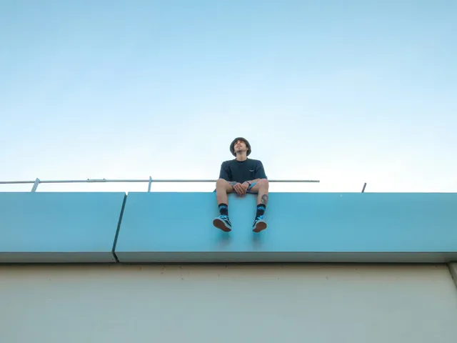 A person sitting on the edge of a flat roof against a blue sky